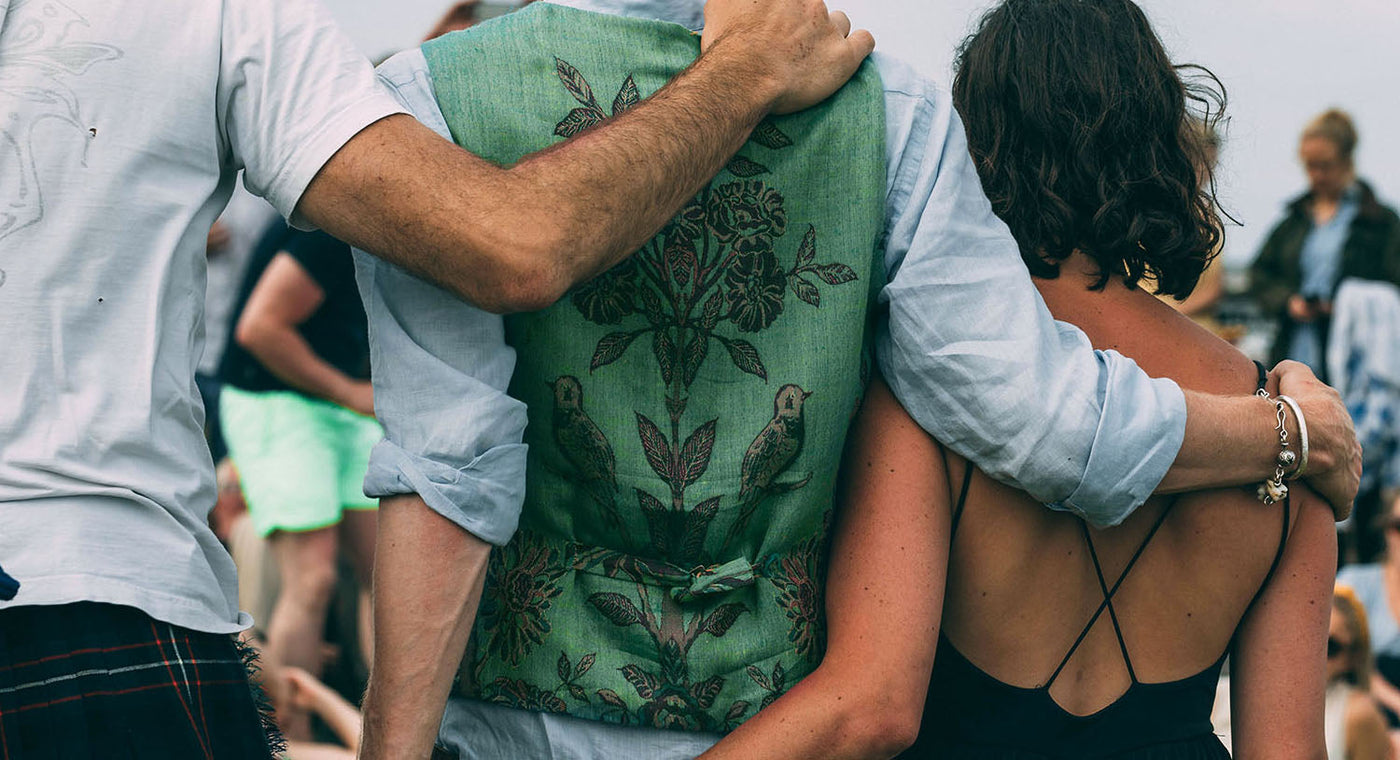 The back of two men and a woman with their arms around each other, the man in the centre wears a pale green cashmere mens waistcoat by shibumi. 