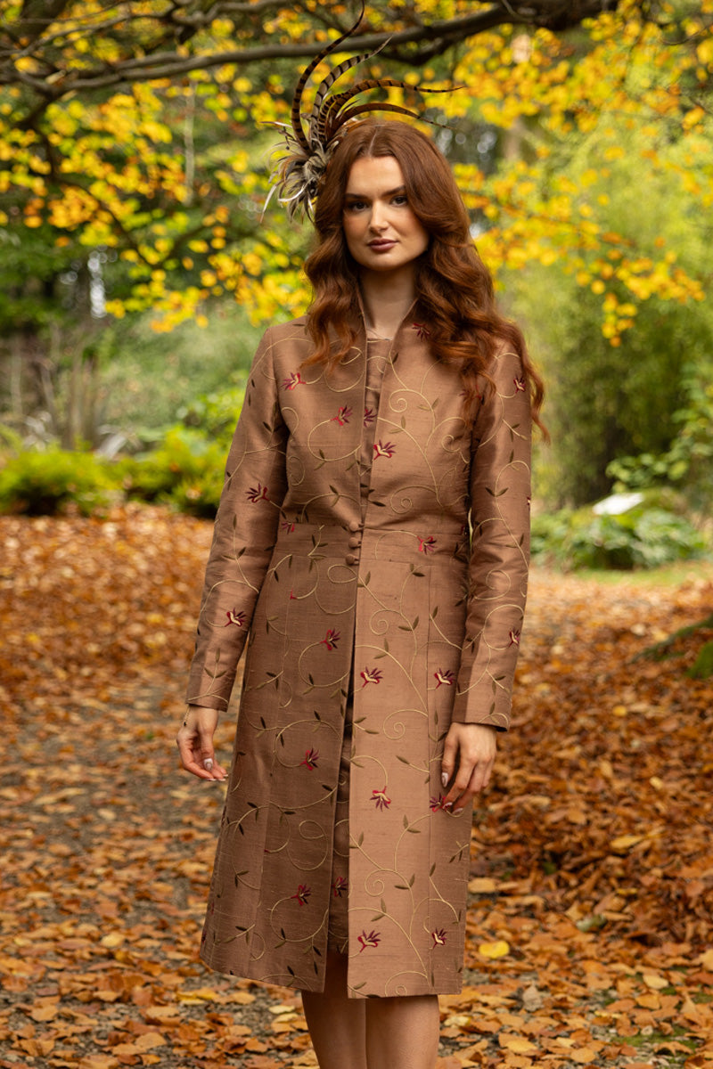 Women's dress coat in brown silk with three buttons at the front. The fabric has soft embroidery in gold and red. Matched with same fabric dress. Both Raphaelite Brown by Shibumi.