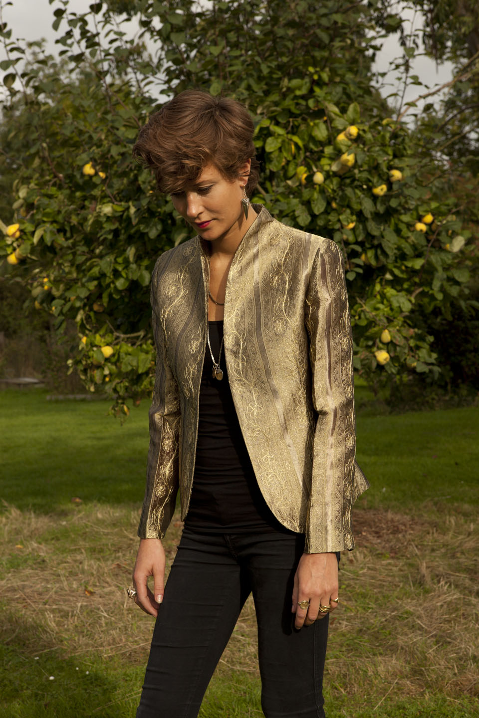 Young woman standing in front of a tree, wearing gold coloured jacket.