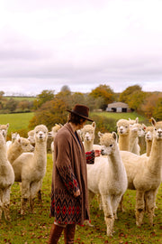 Woman wearing long brown wool coat playing with alpacas. 