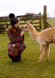 Alpaca sniffing a girl's hand who is wearing alpaca wool eco cardigan. 
