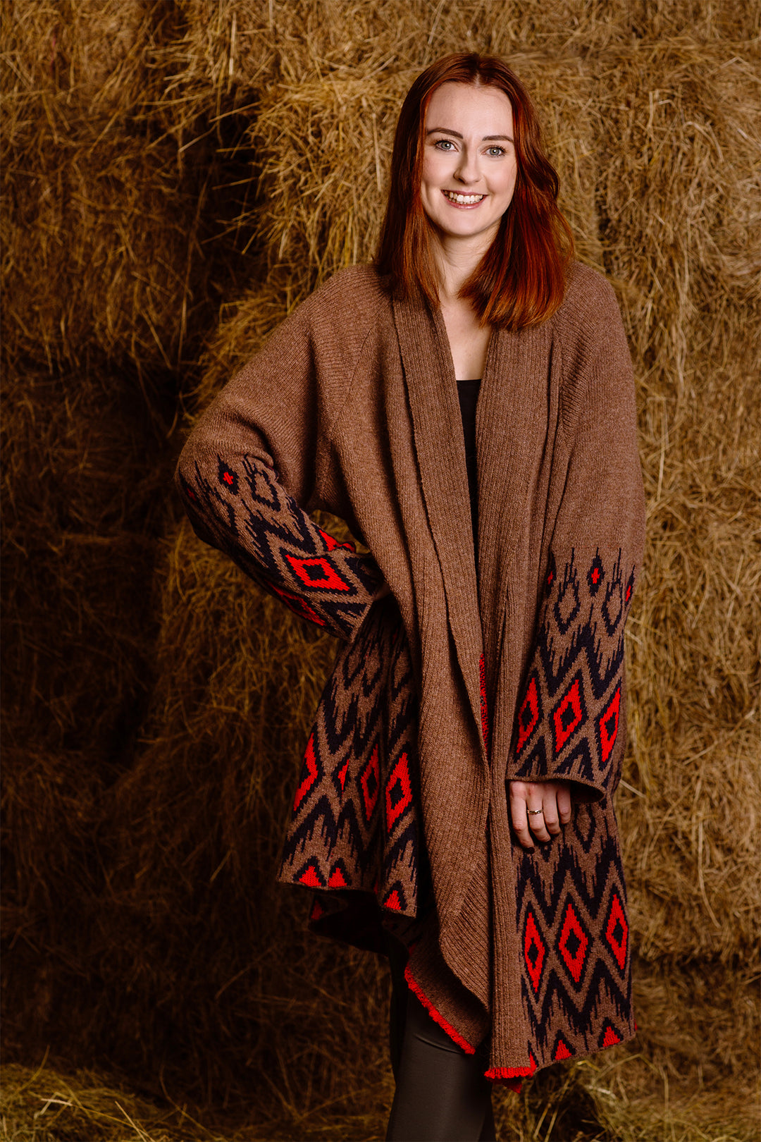 Young woman standing in a barn, wearing brown wool coat with native motives.