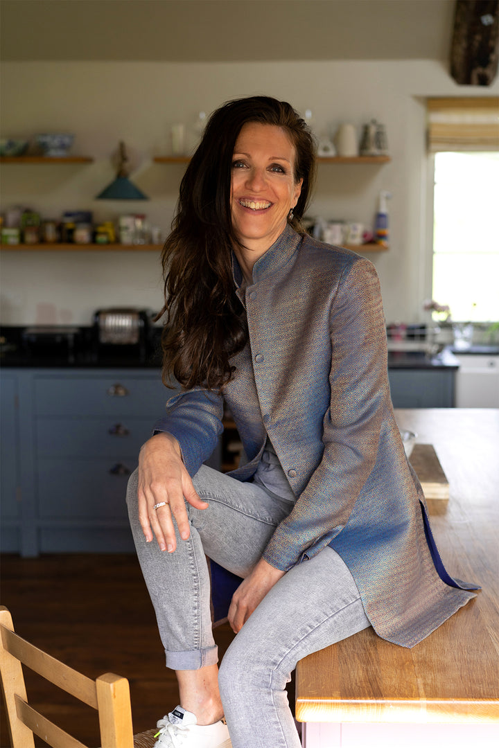 Lady sitting on a kitchen table wearing geo pattern blue jacket.