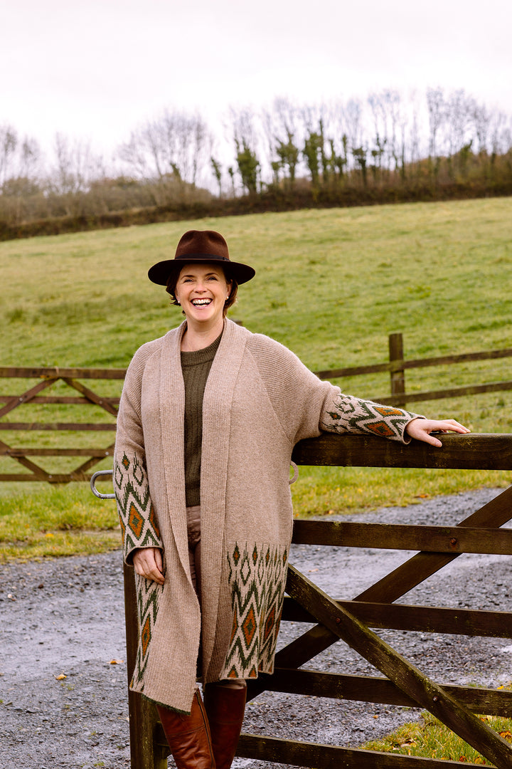 Lady smiling at the side of a field, wearing long wool cardigan.