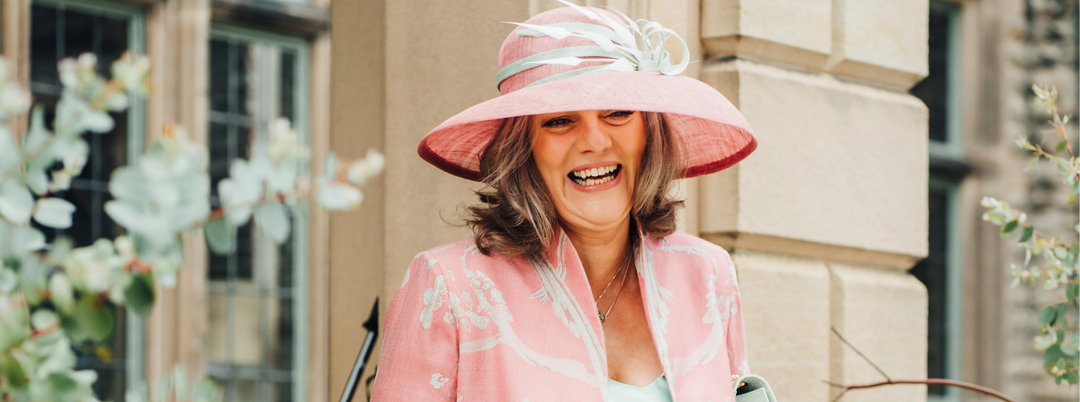 Mother of the Bride wearing a pink embroidered silk coat and coordinating hat at a summer wedding