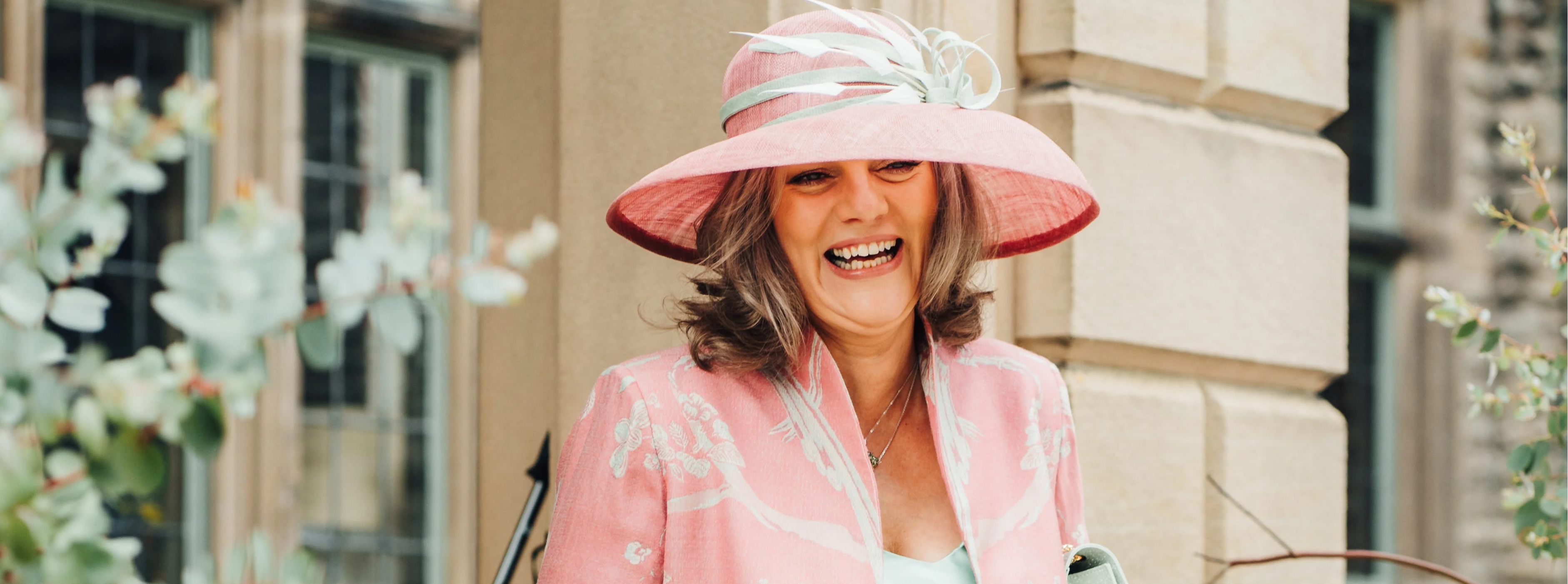 Mother of the Bride wearing a pink embroidered silk coat and coordinating hat at a summer wedding