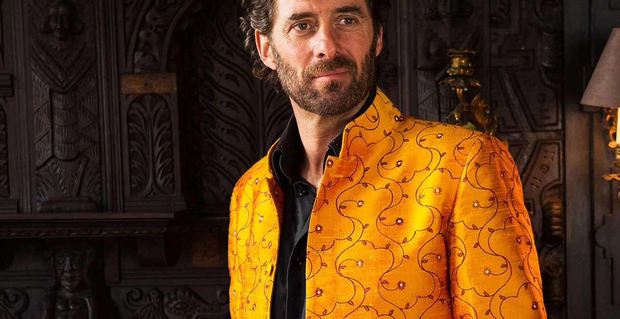 A man with dark hair in a smart colourful men's outfit with a silk men's nehru jacket in embroidered gold silk
