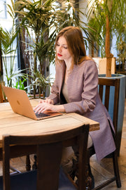 young woman sitting in a restaurant working on her laptop wearing a fitted shibumi jacket in copper rose 