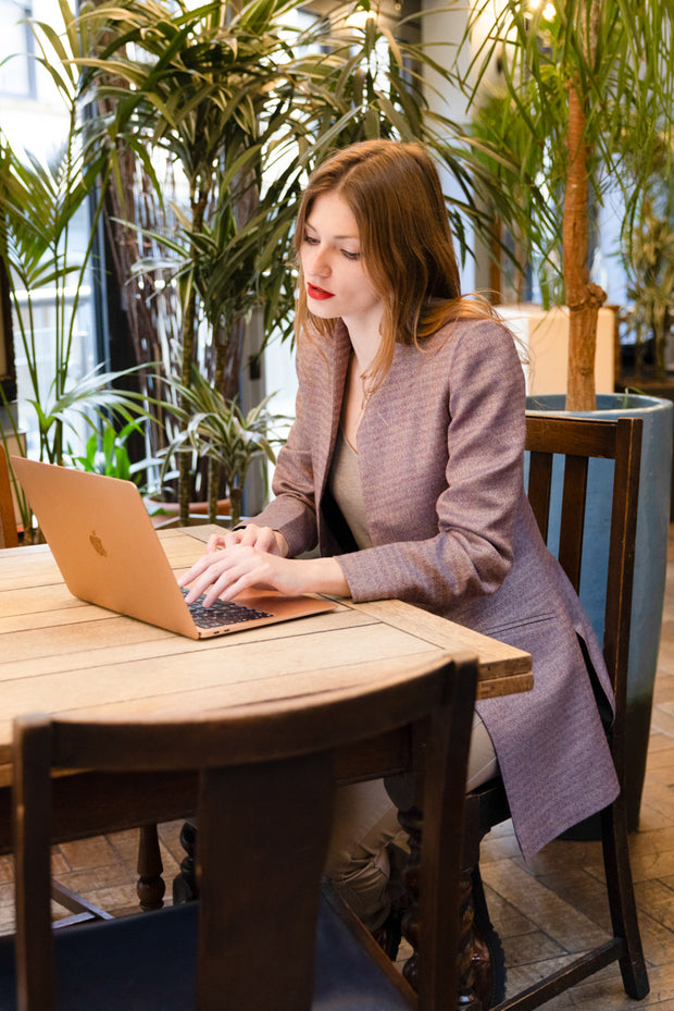 young woman sitting in a restaurant working on her laptop wearing a fitted shibumi jacket in copper rose 