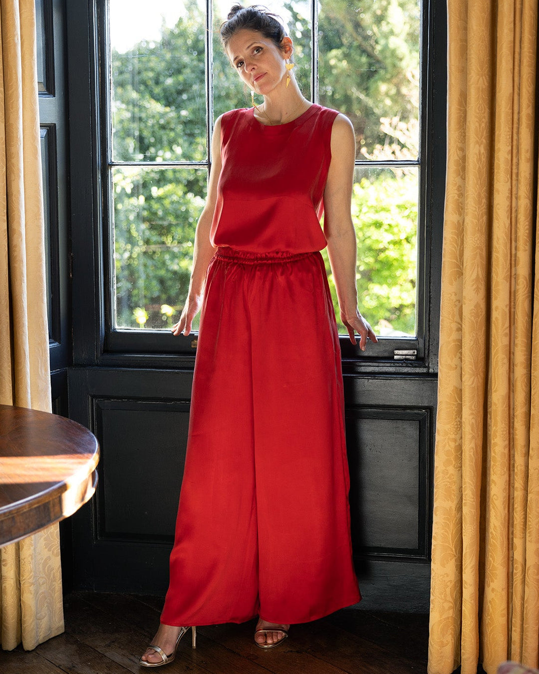 Woman in a red dress standing in a room with large windows and yellow curtains.