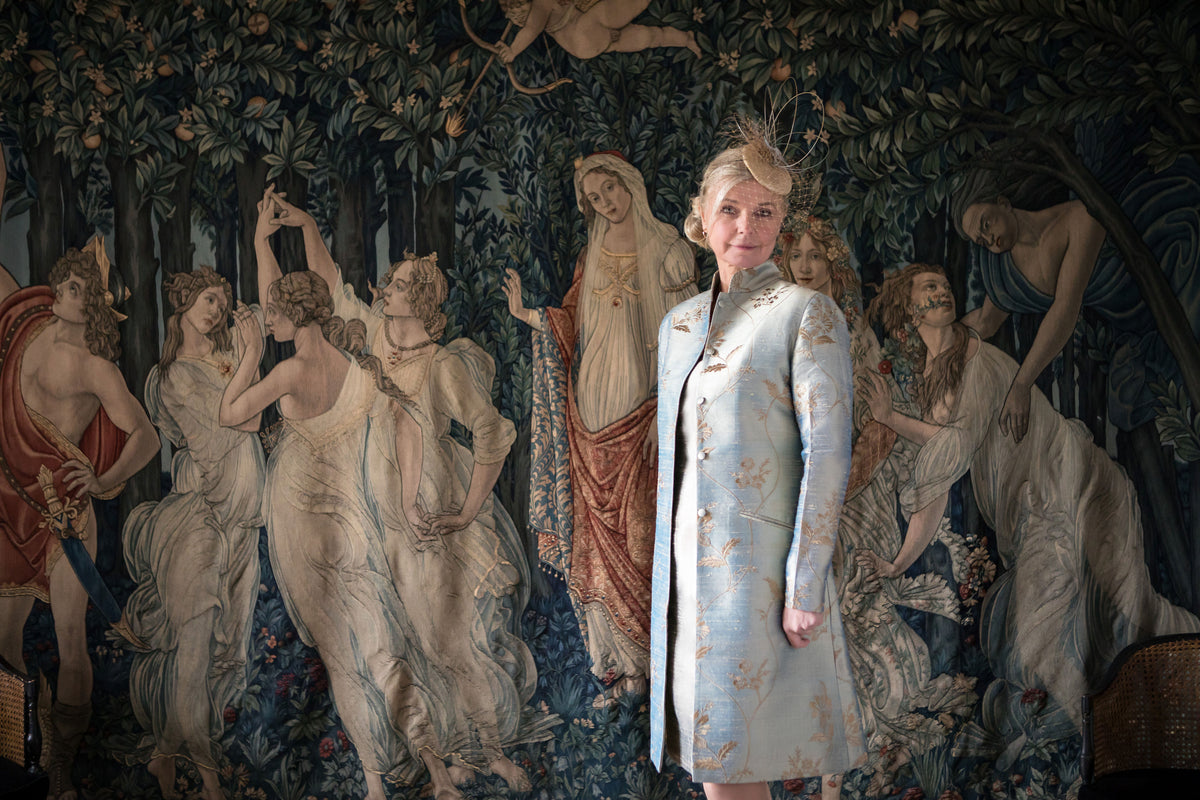 Woman standing in front of a tapestry with classical scenes wearing a shibumi garment