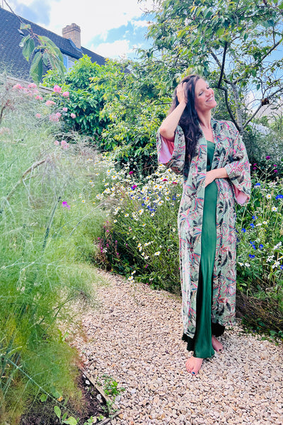 Woman in botanical garden surrounded by blooming flowers, wearing a silk velvet dressing gown in a sumptuous botanical green silk velvet printed with a rich floral design