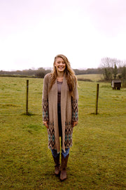 Young woman standing at the field wearing a long cardigan with native pattern