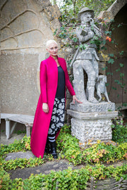 Lady standing next to a statue wearing bright long pink coat. 