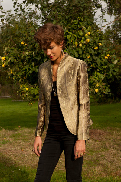 Young woman standing in front of a tree, wearing gold coloured jacket. 