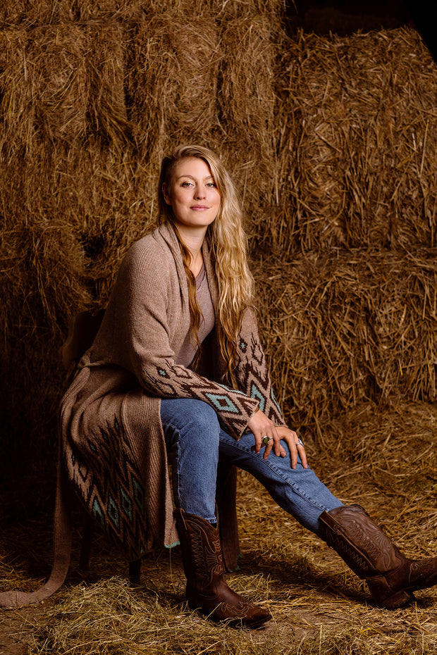 Woman wearing aqua brown natural wool coat, sitting in the barn. 
